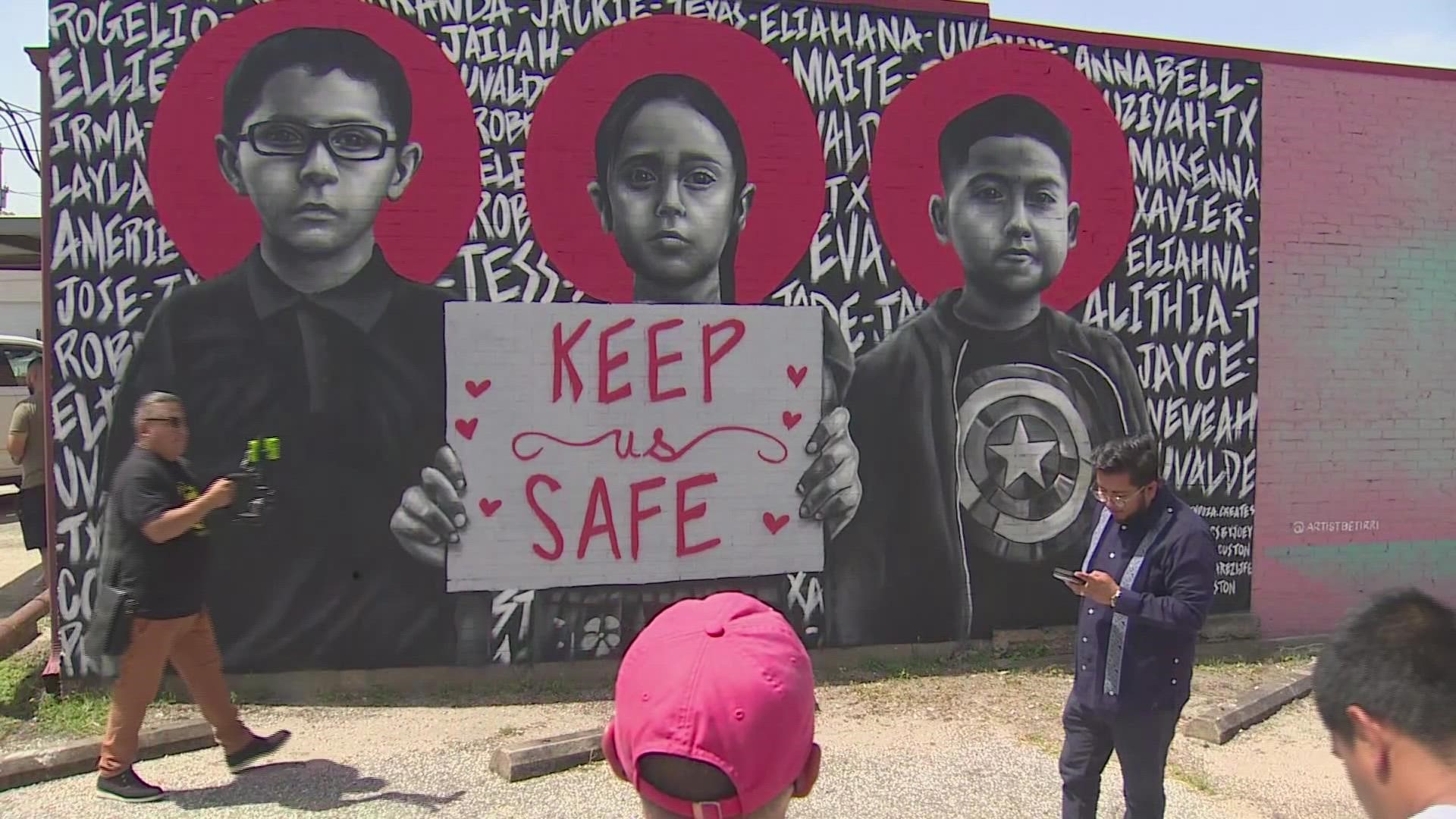 In the mural, three children are holding a sign reading 'Keep us safe.' It also has the names of the 21 people killed that day.